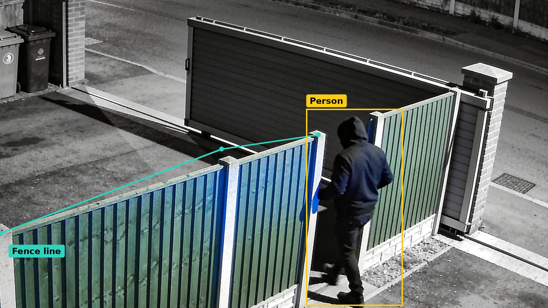 Infrared CCTV of a side gate at night: a teal line along the fence top and a person boxed in amber