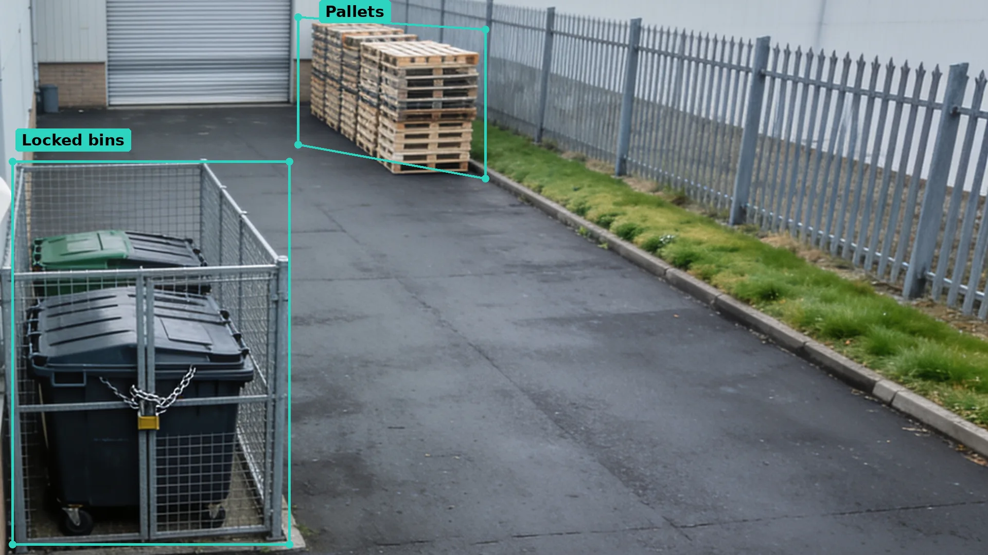 Daytime CCTV of a tidy yard: bins locked in a mesh cage and pallets by the far fence, each in a teal zone