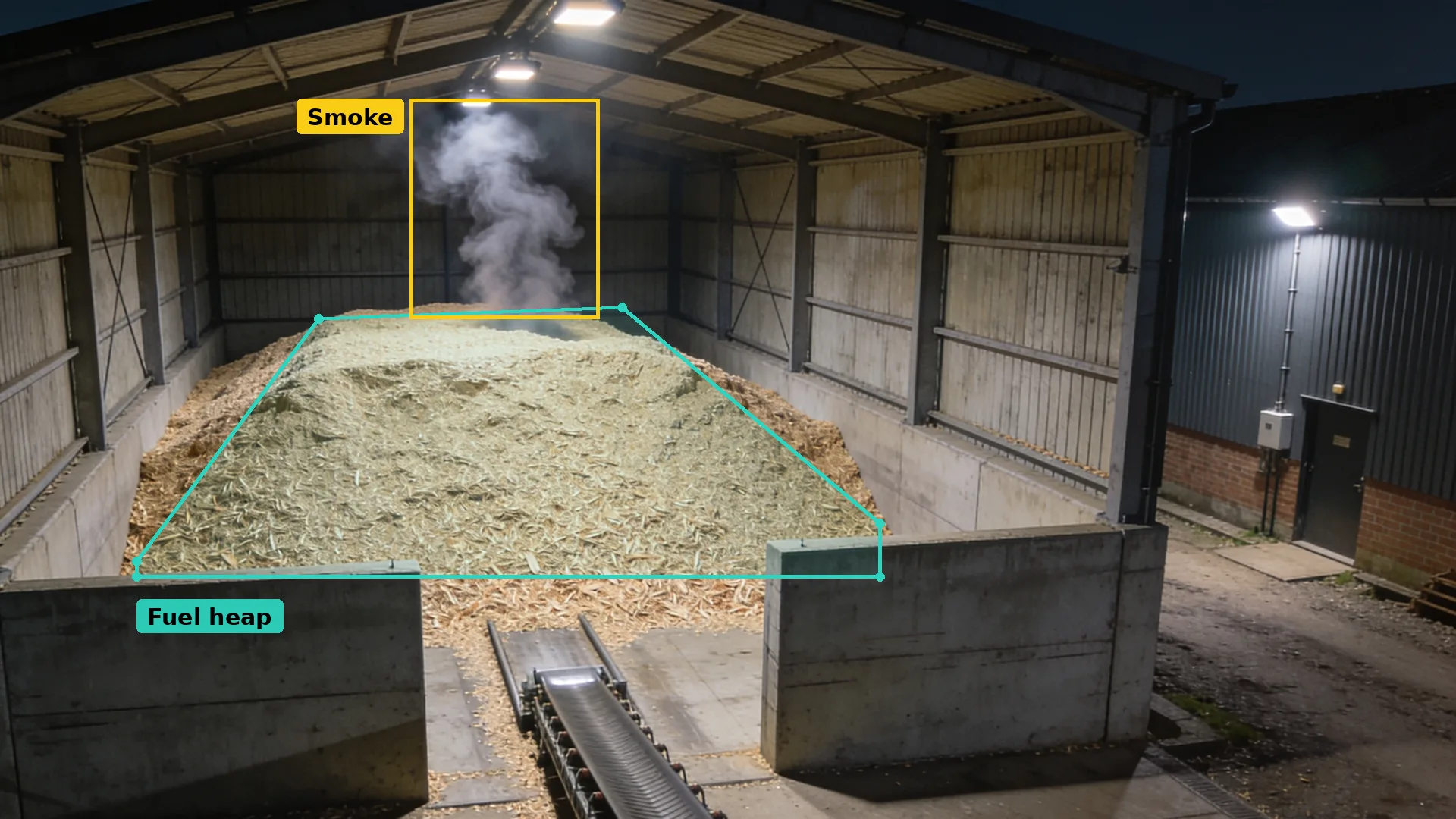 Night CCTV inside a wood chip store: the heap in a teal zone and a plume of smoke boxed in amber above it