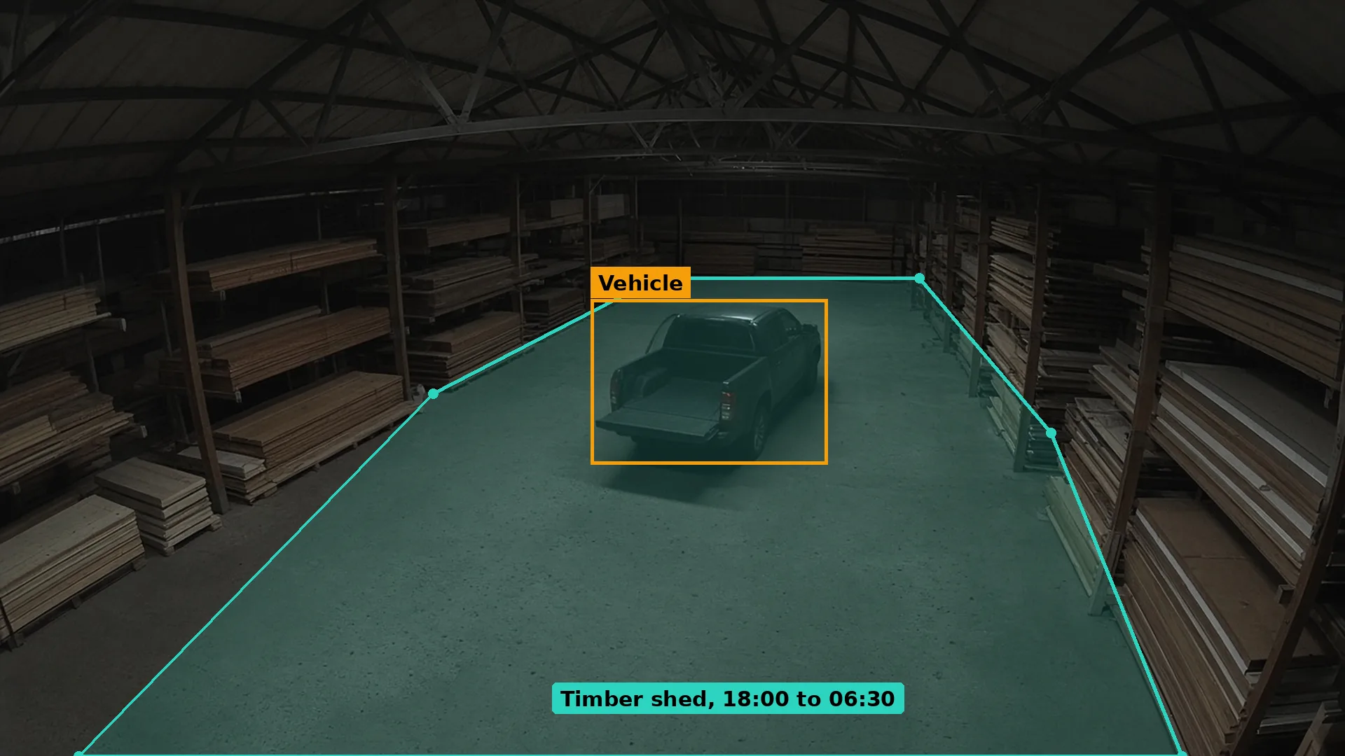 Night CCTV of a pickup stopped inside an open-sided timber shed between racks of sawn timber, boxed in amber