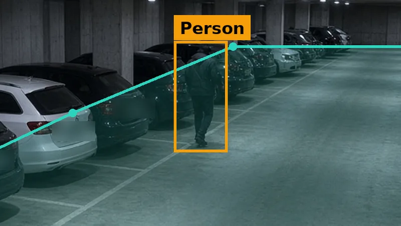 Phone alert crop: a hooded figure between parked cars on a car park deck at night, boxed in amber