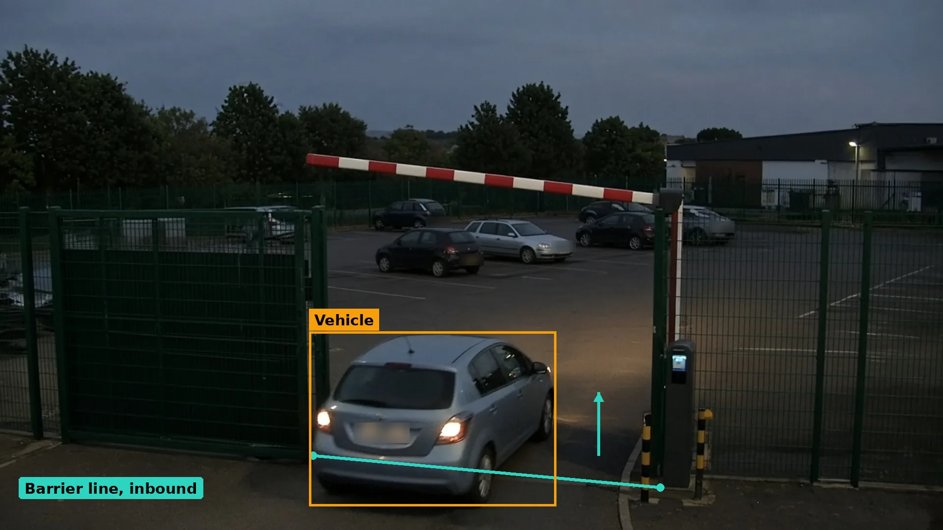 Dusk CCTV of a car passing a raised barrier into a fenced staff car park, a teal inbound line, the car boxed