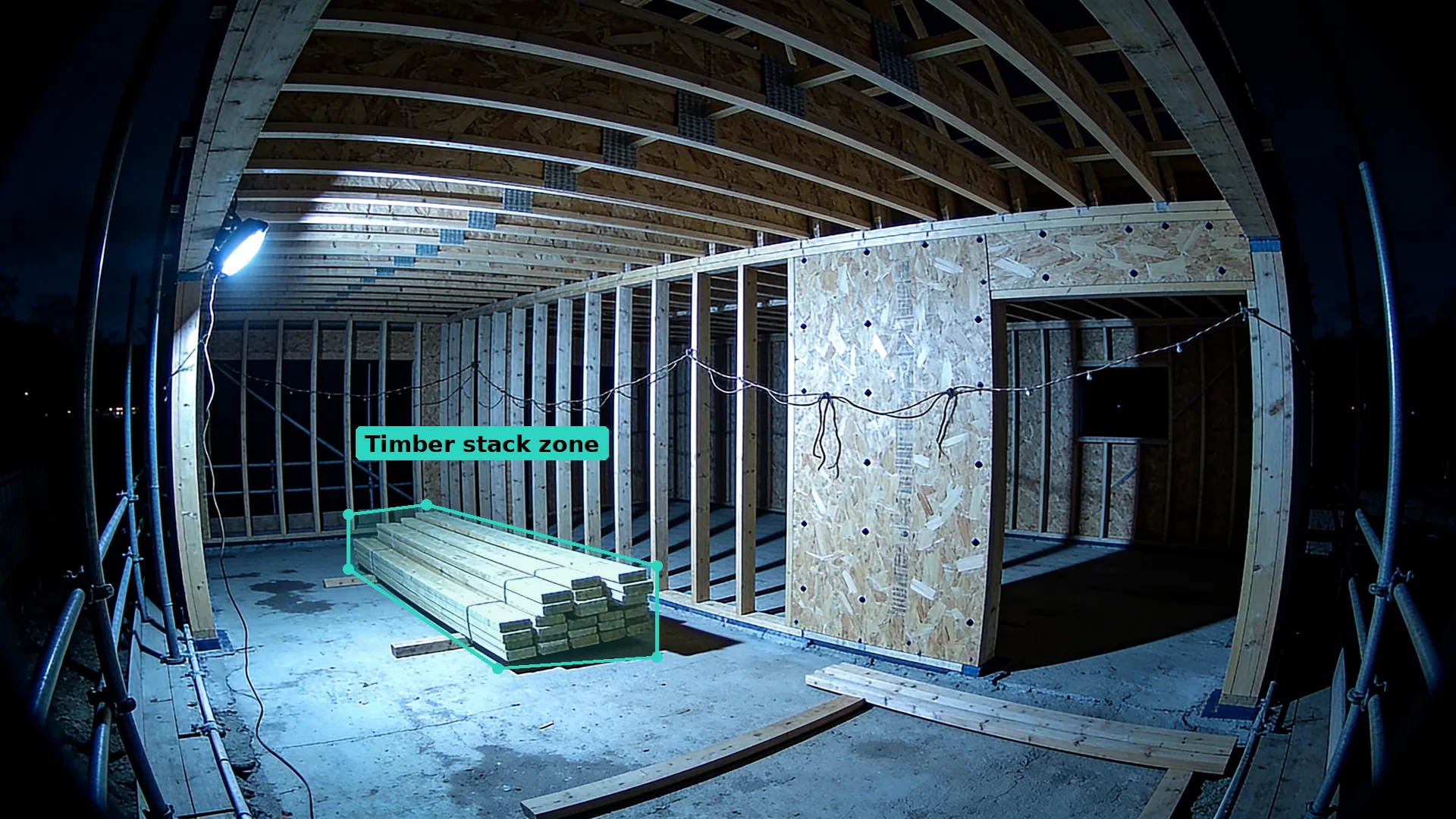 Night CCTV inside a timber frame house under construction, a stack of studs on the slab inside a teal zone