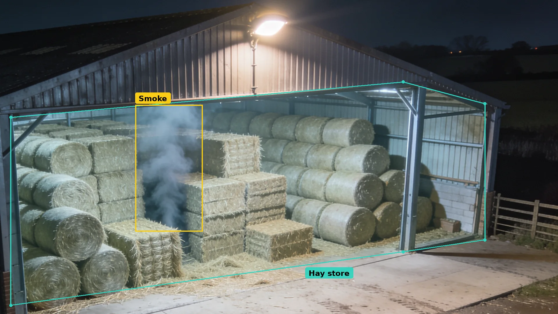 Night CCTV of a hay barn: smoke rising from stacked bales boxed in amber, the stack inside a teal zone