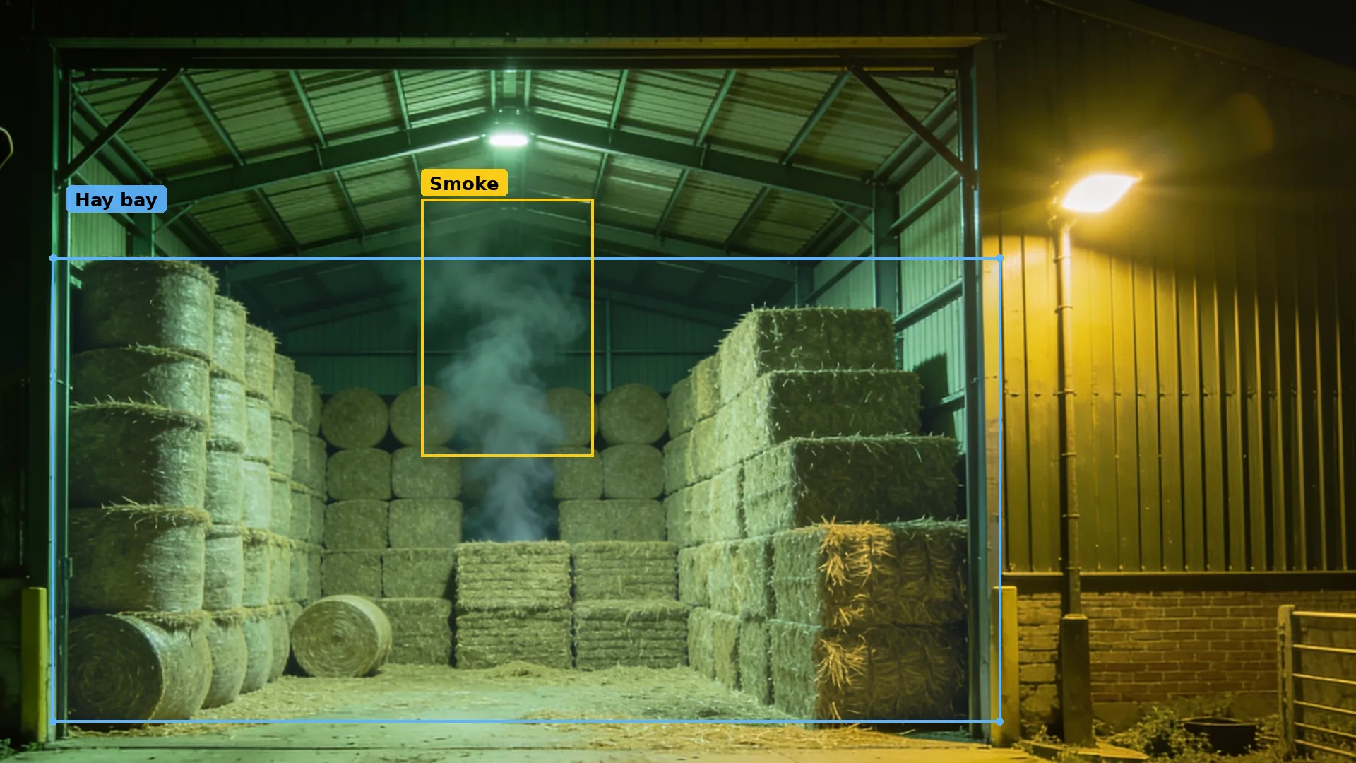 CCTV of a hay bay with large bales in a blue zone and a thin wisp of smoke rising from the stack, boxed
