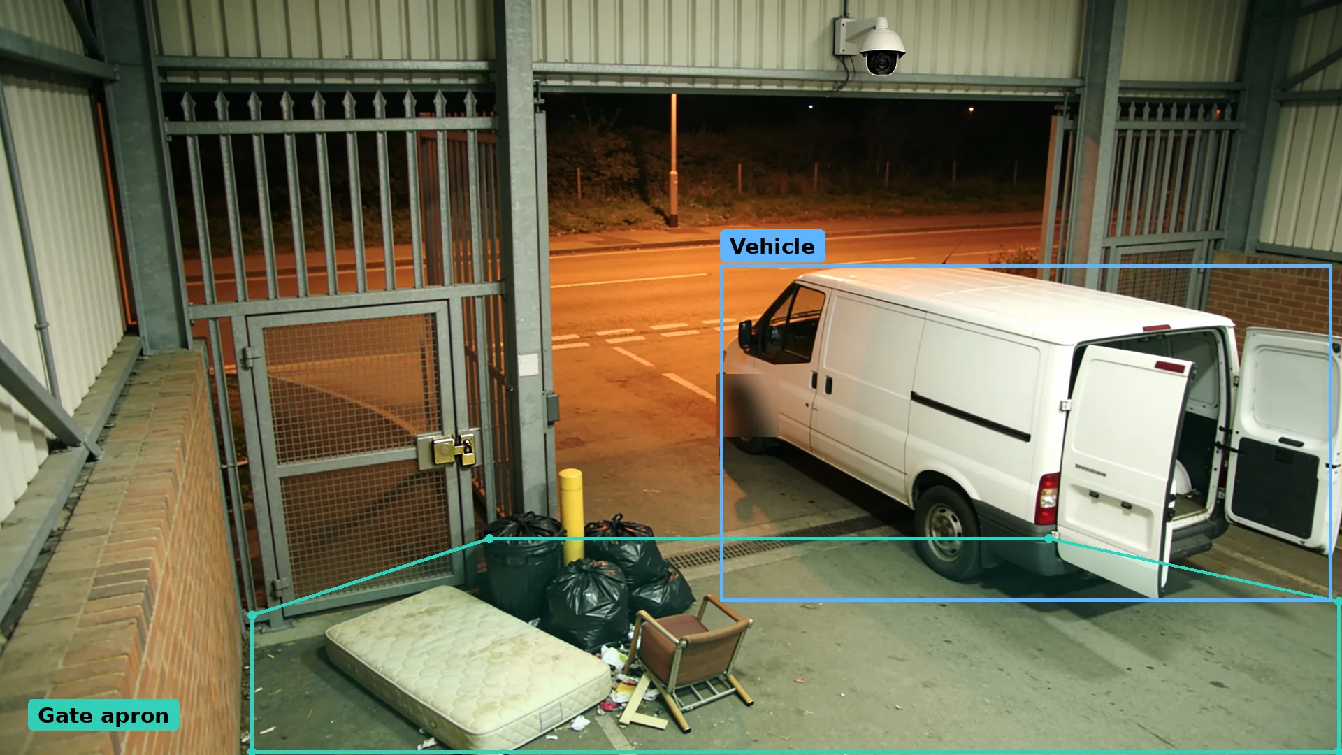 Night CCTV outside a locked recycling centre gate: a van boxed in blue beside dumped bags and a mattress, plate blurred