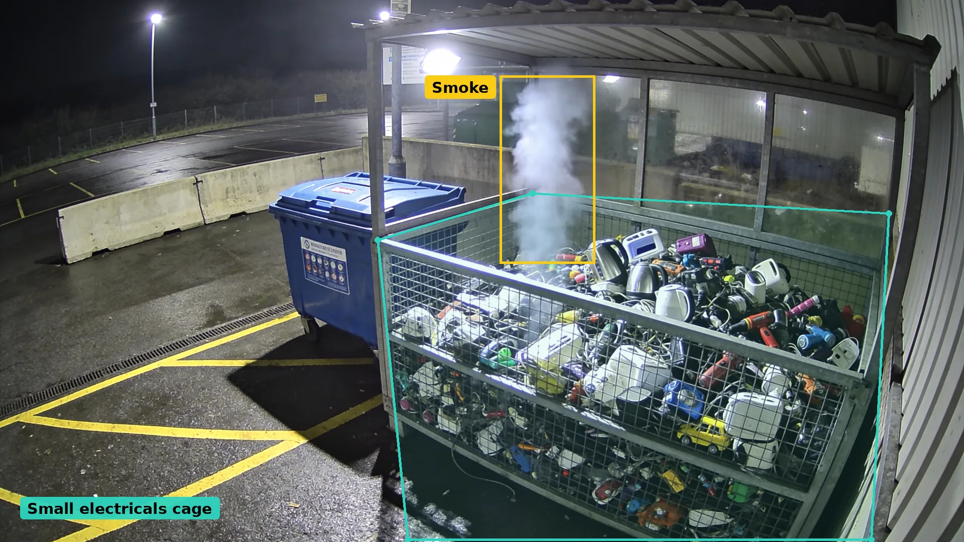 Night CCTV of a recycling centre small electricals cage in a teal zone, with rising smoke boxed in amber