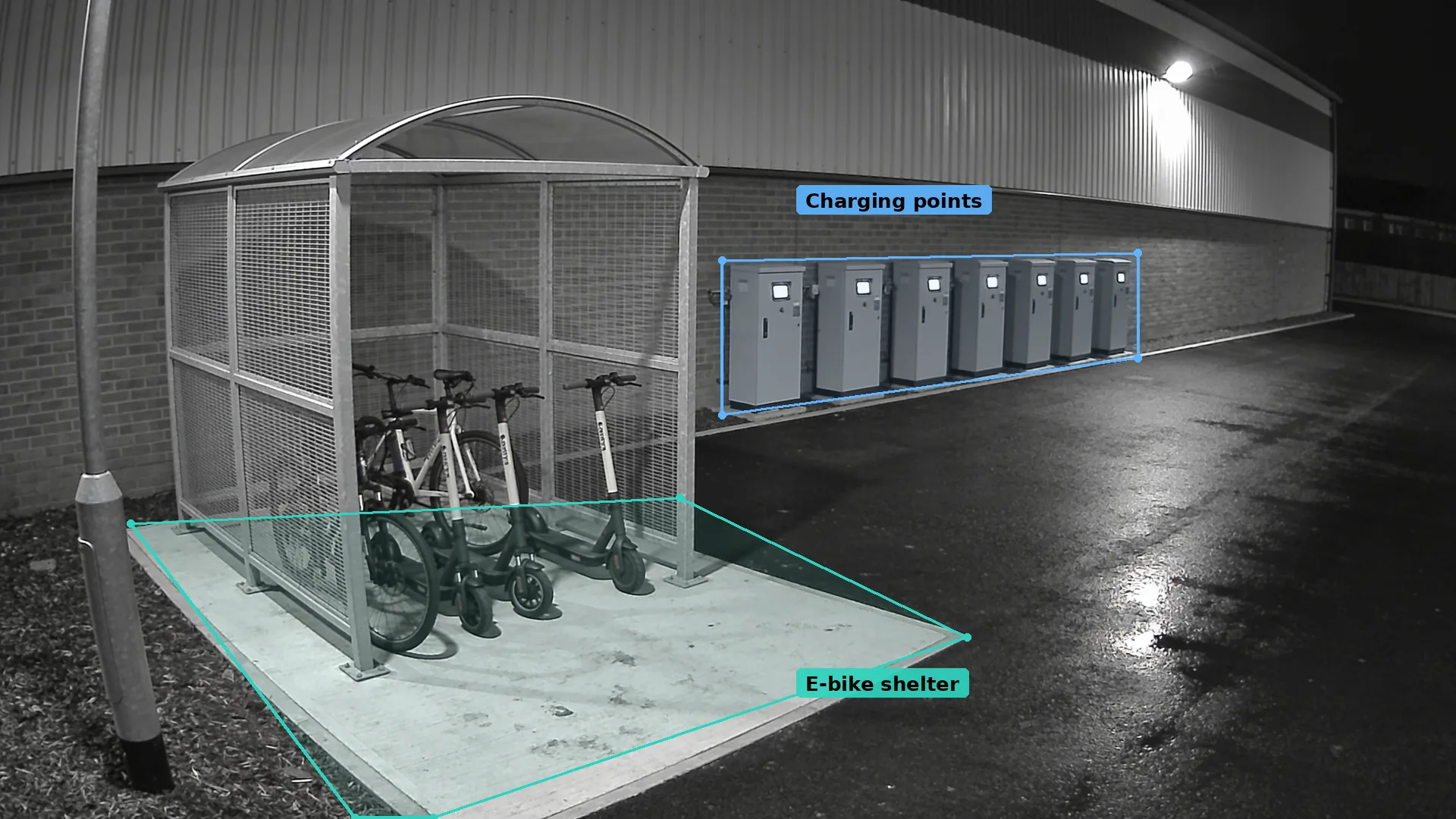 Night CCTV of an outdoor cycle shelter with e-bikes and e-scooters in a teal zone, and wall charging points in blue