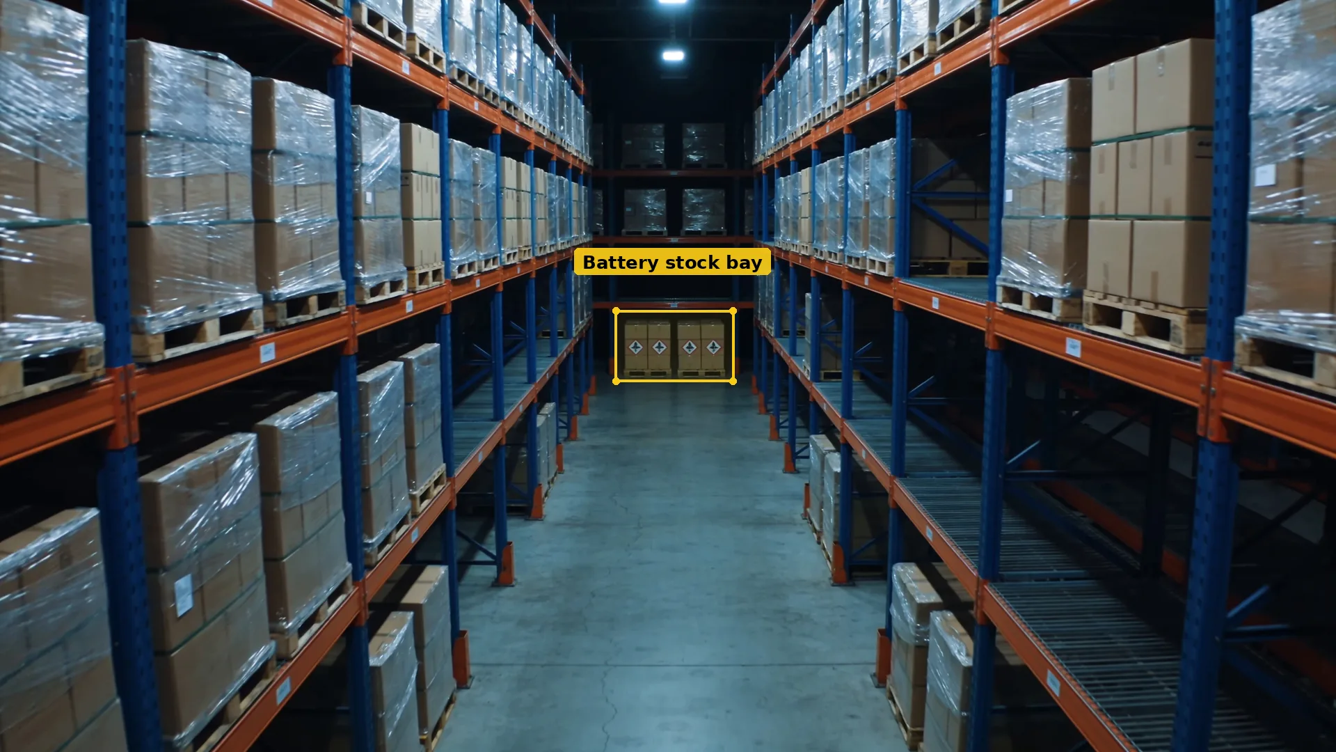 Night CCTV of a warehouse racking aisle, with a separate bay of hazard-labelled battery cartons boxed in amber at the end
