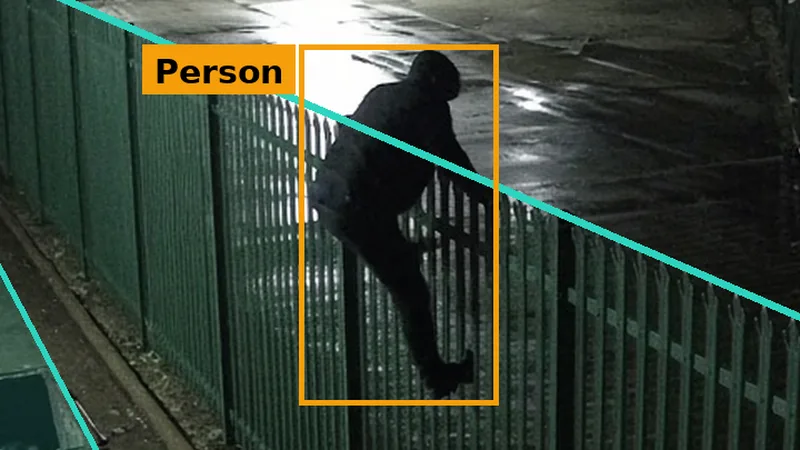 Phone alert crop: a figure on an industrial palisade fence at night, crossing a teal fence line