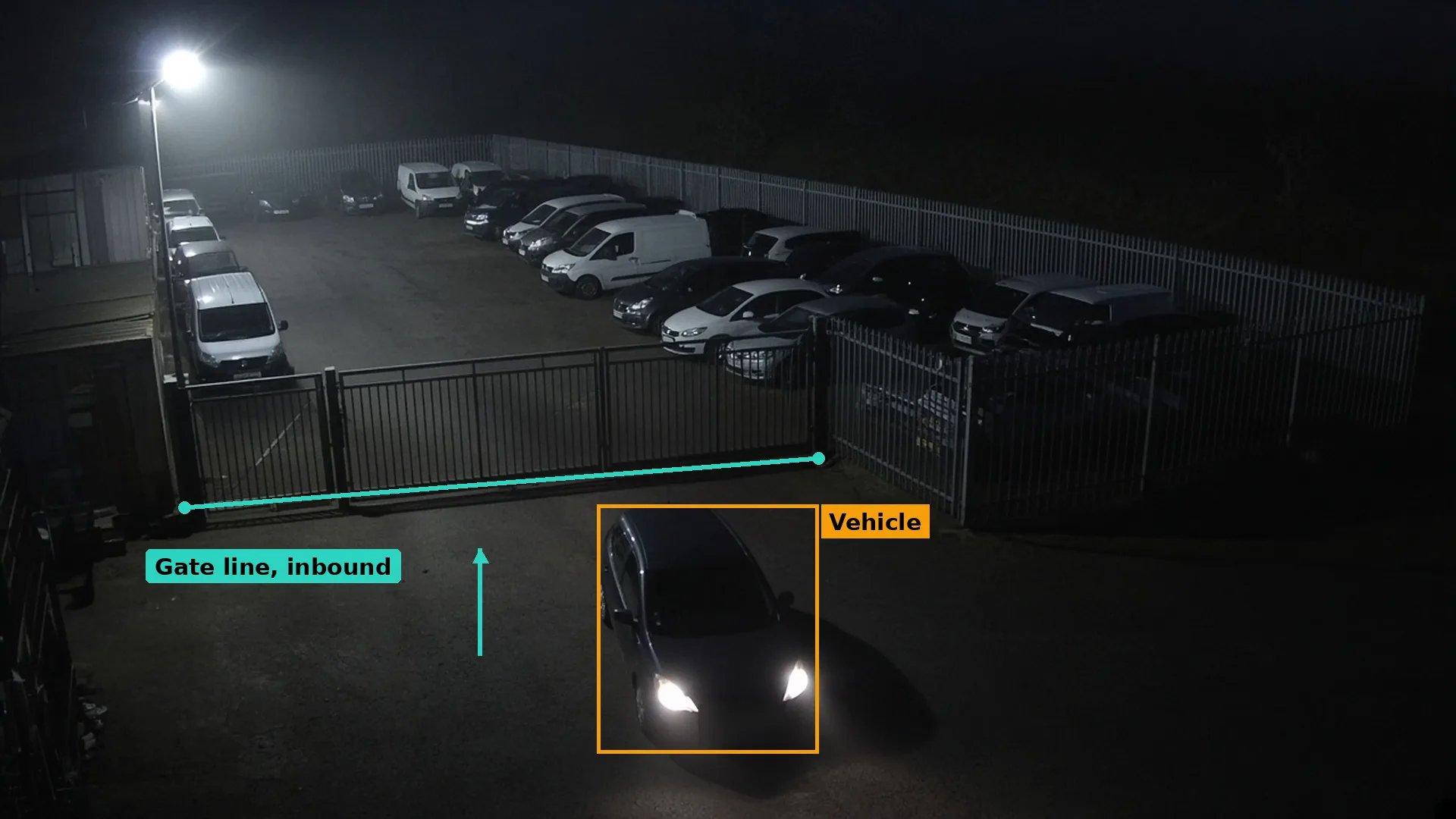 Night CCTV of a car stopped at the closed gate of a vehicle storage yard, a teal gate line and the car boxed