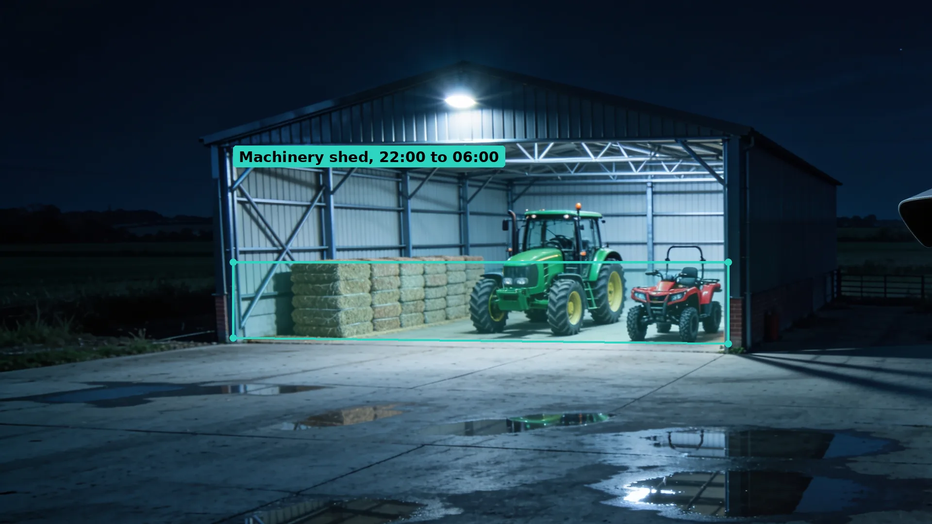 Night CCTV of an open-fronted farm shed with a green tractor and a red quad bike by stacked bales, the floor in a teal zone
