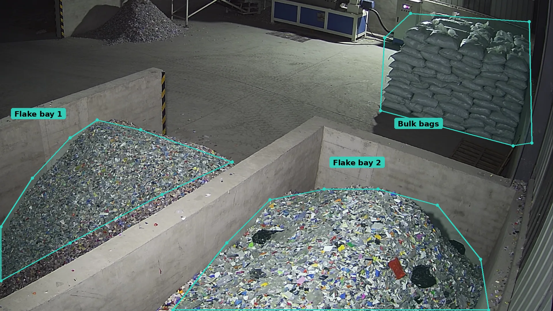 Night CCTV inside a plastics shed: teal zones round two concrete bays of plastic flake and a stack of bulk bags