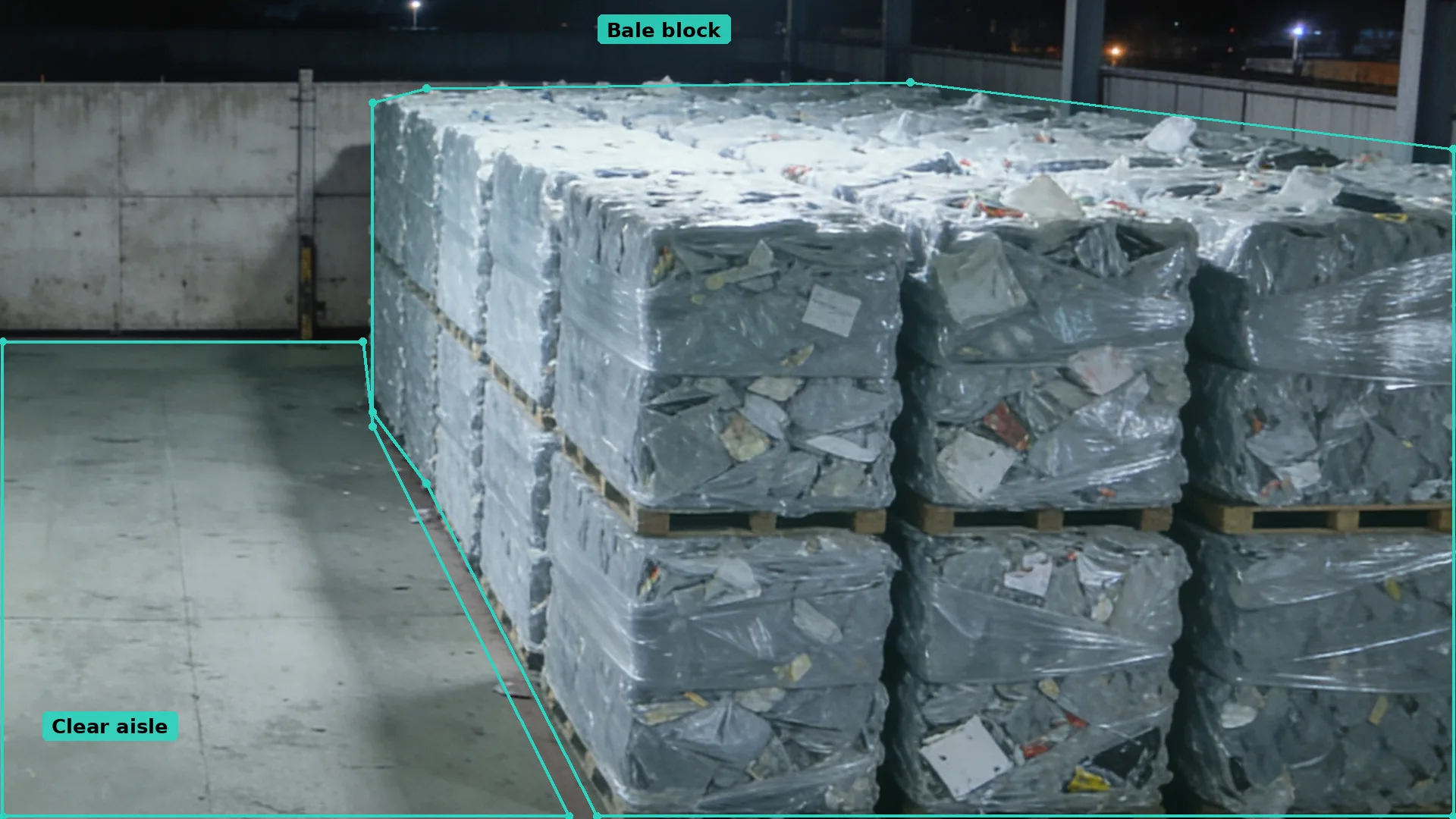 Night CCTV inside a fuel bale store: a teal zone round a block of wrapped bales and another round the clear aisle beside it