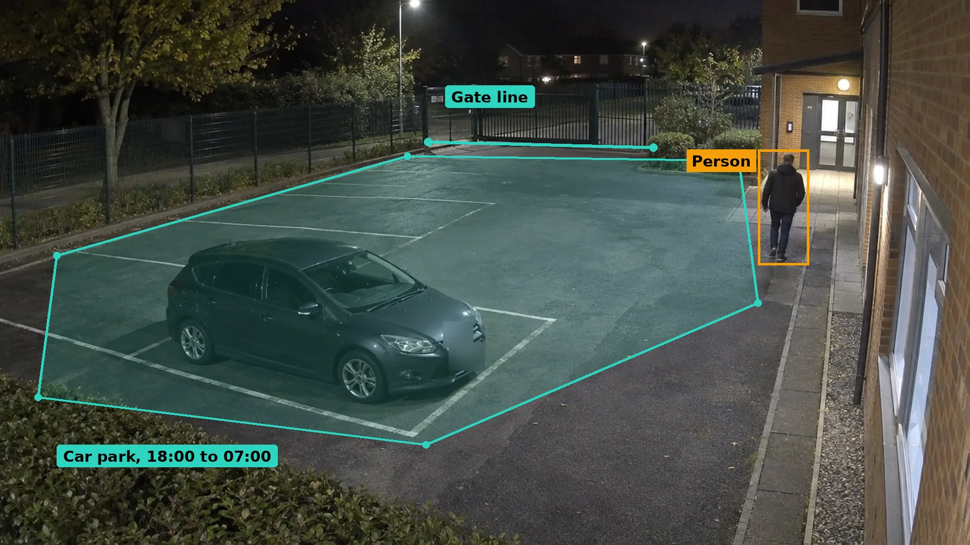 Night CCTV of a school staff car park with one parked car and an adult walking towards a side entrance, boxed in amber