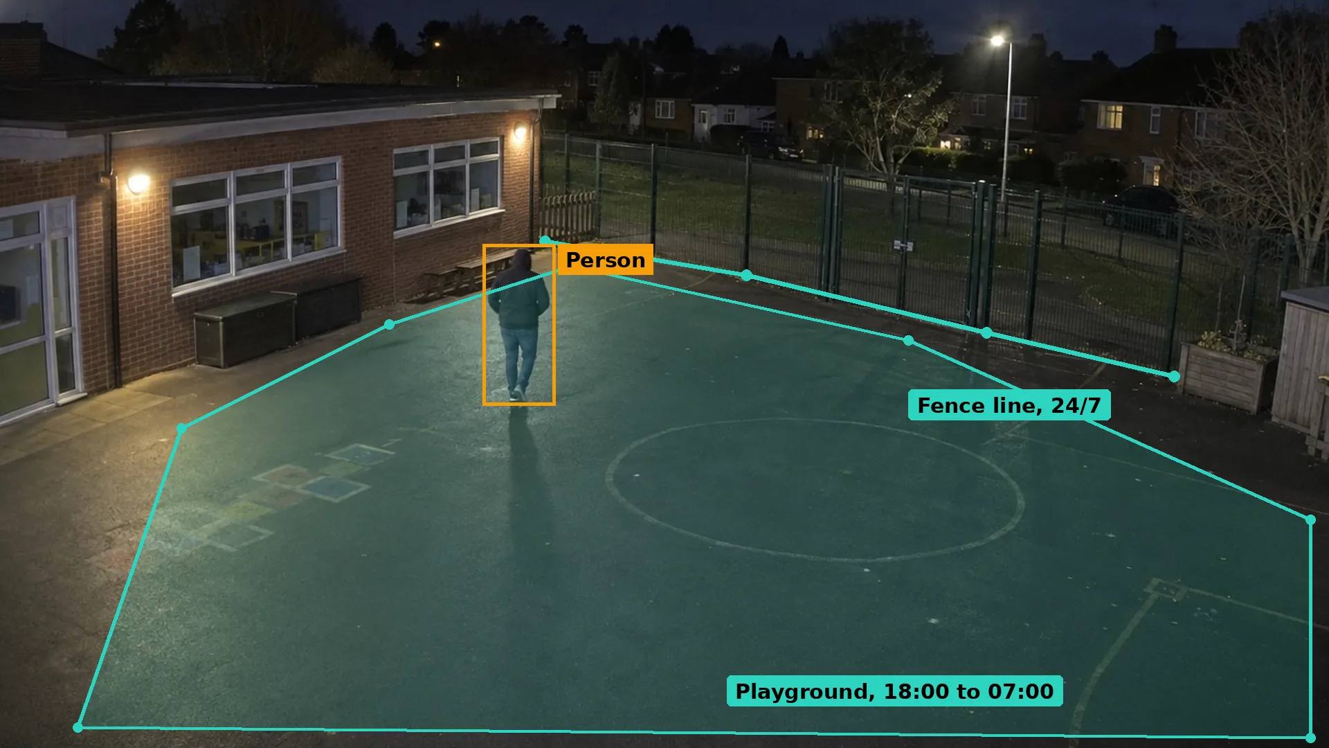 Night CCTV of a hooded adult walking across an empty primary school playground towards the classrooms, boxed in amber