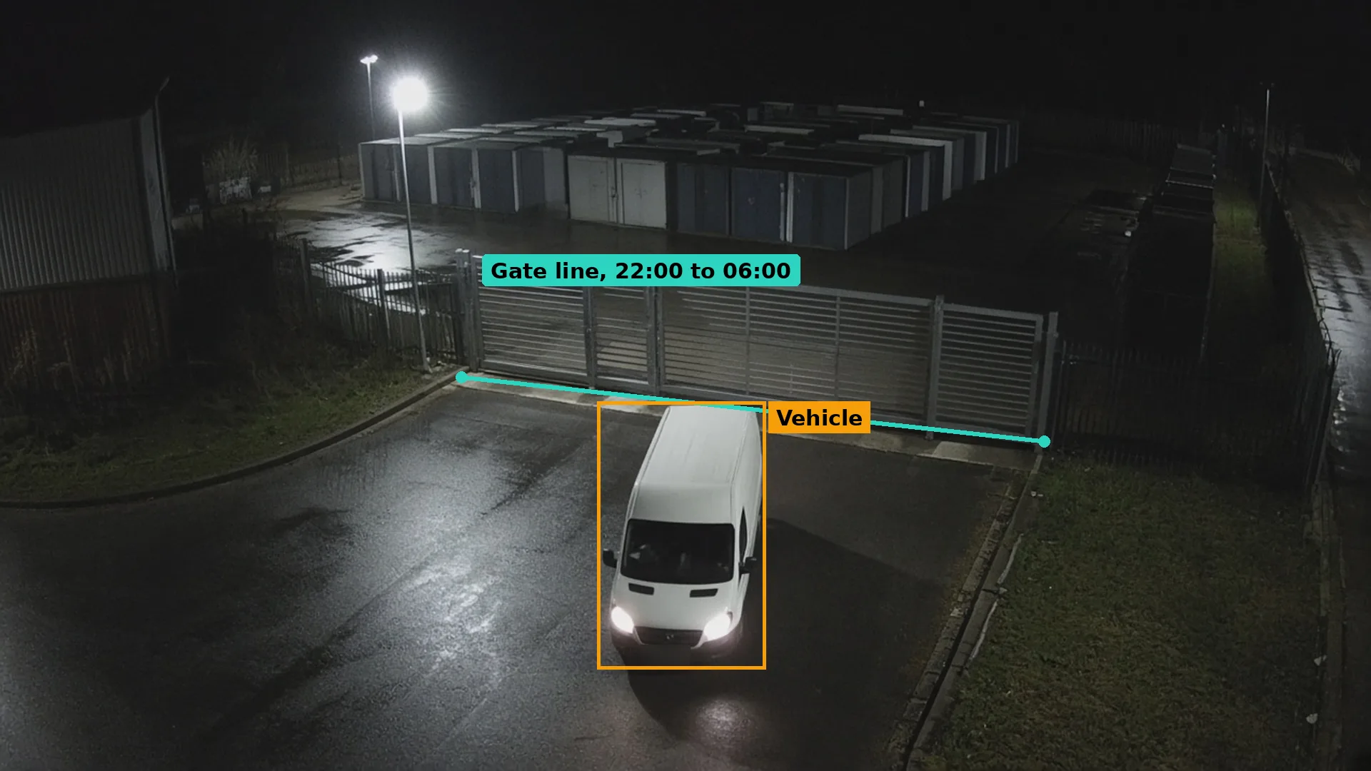 Night CCTV of a white van stopped facing a closed sliding gate at a self-storage site, boxed in amber