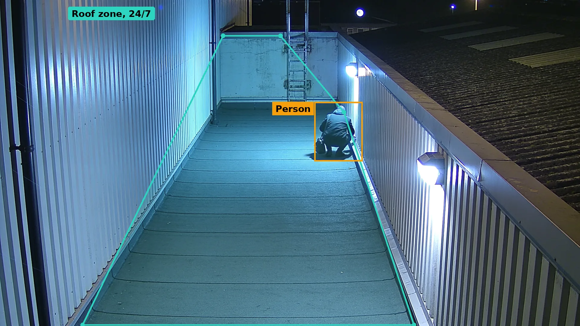 Night CCTV of a roof walkway on an empty unit, a crouching person boxed in amber inside a teal roof zone