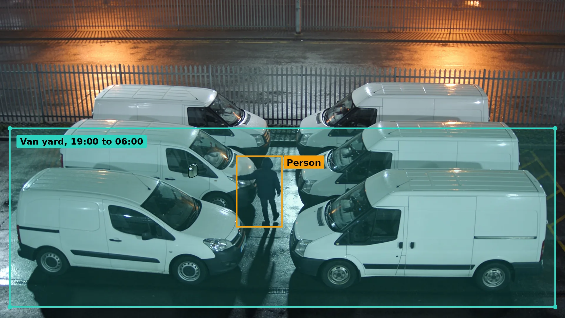 Night CCTV of a person walking between rows of parked white vans in a fenced depot and reaching to a mirror, boxed in amber
