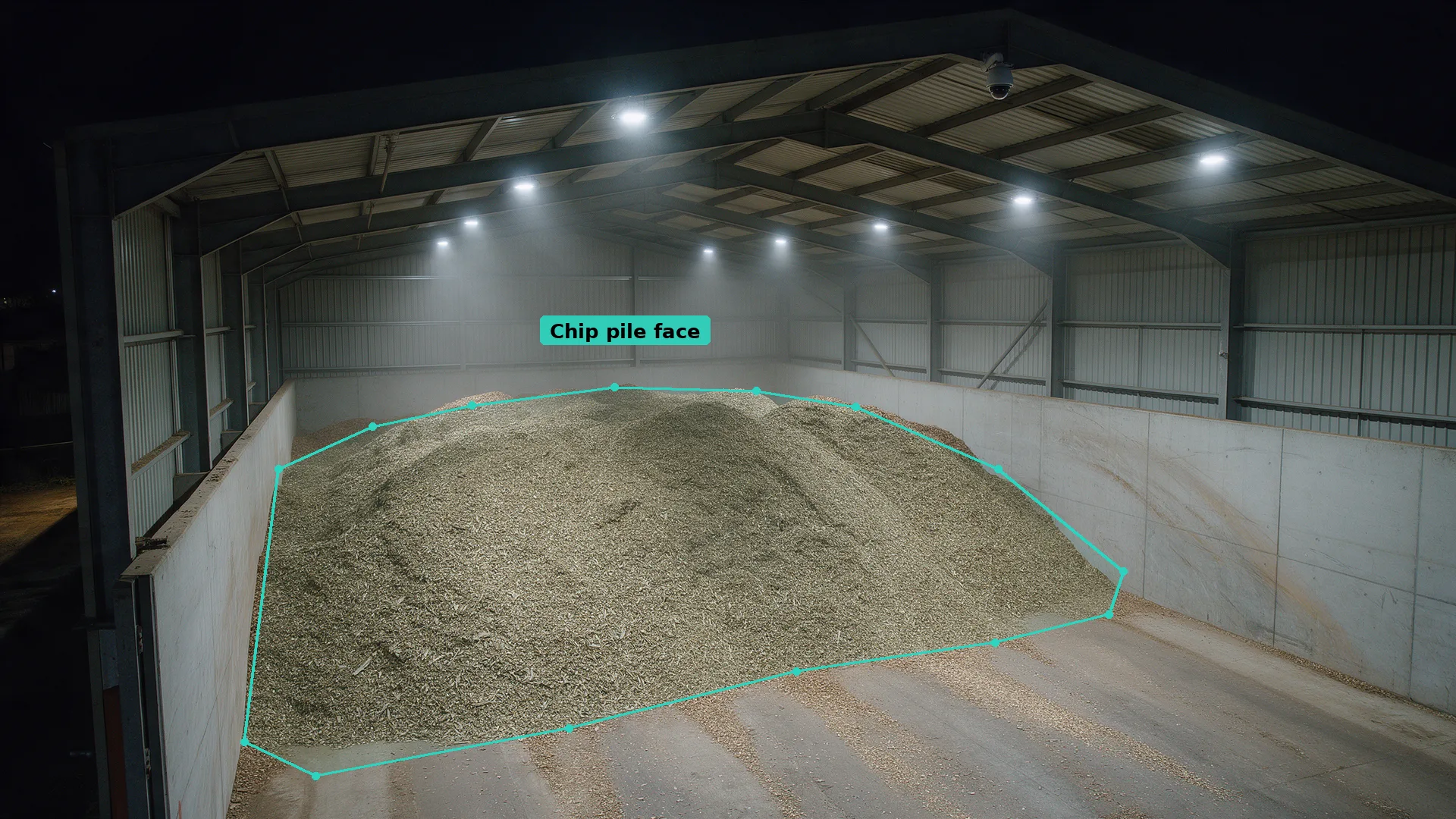 Night CCTV view inside an open-fronted shed holding a large wood chip pile, with a teal detection zone along the pile face