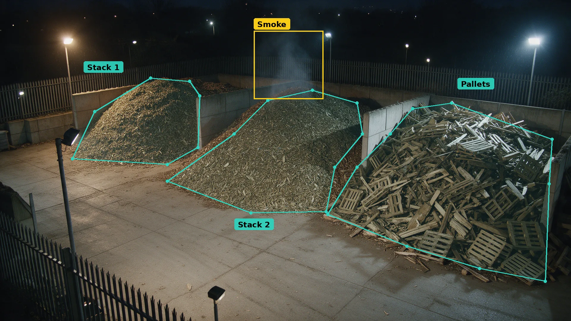 Night CCTV of a waste wood yard: teal zones round three separate stockpiles, smoke boxed in amber on the middle one