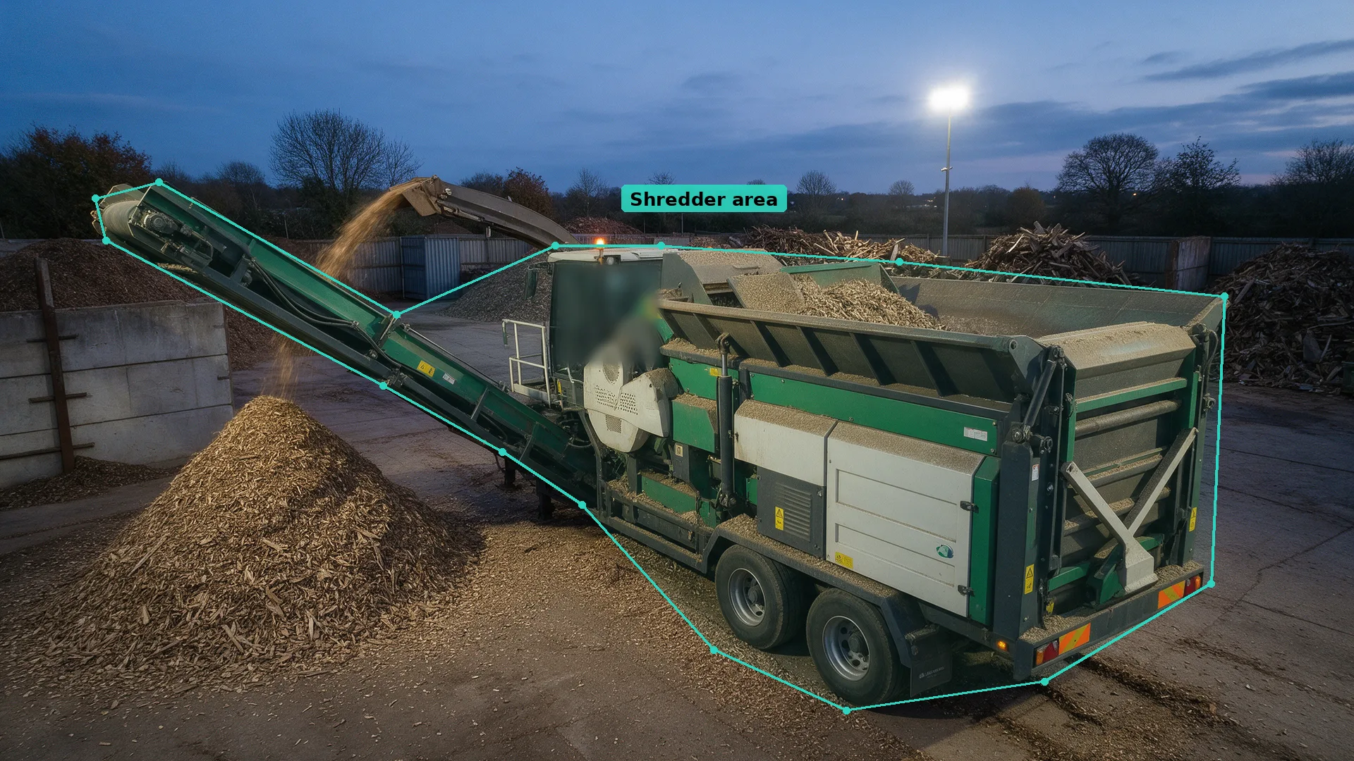 Dusk CCTV view of a mobile wood shredder and conveyor beside a chip pile, outlined by a neat teal detection zone