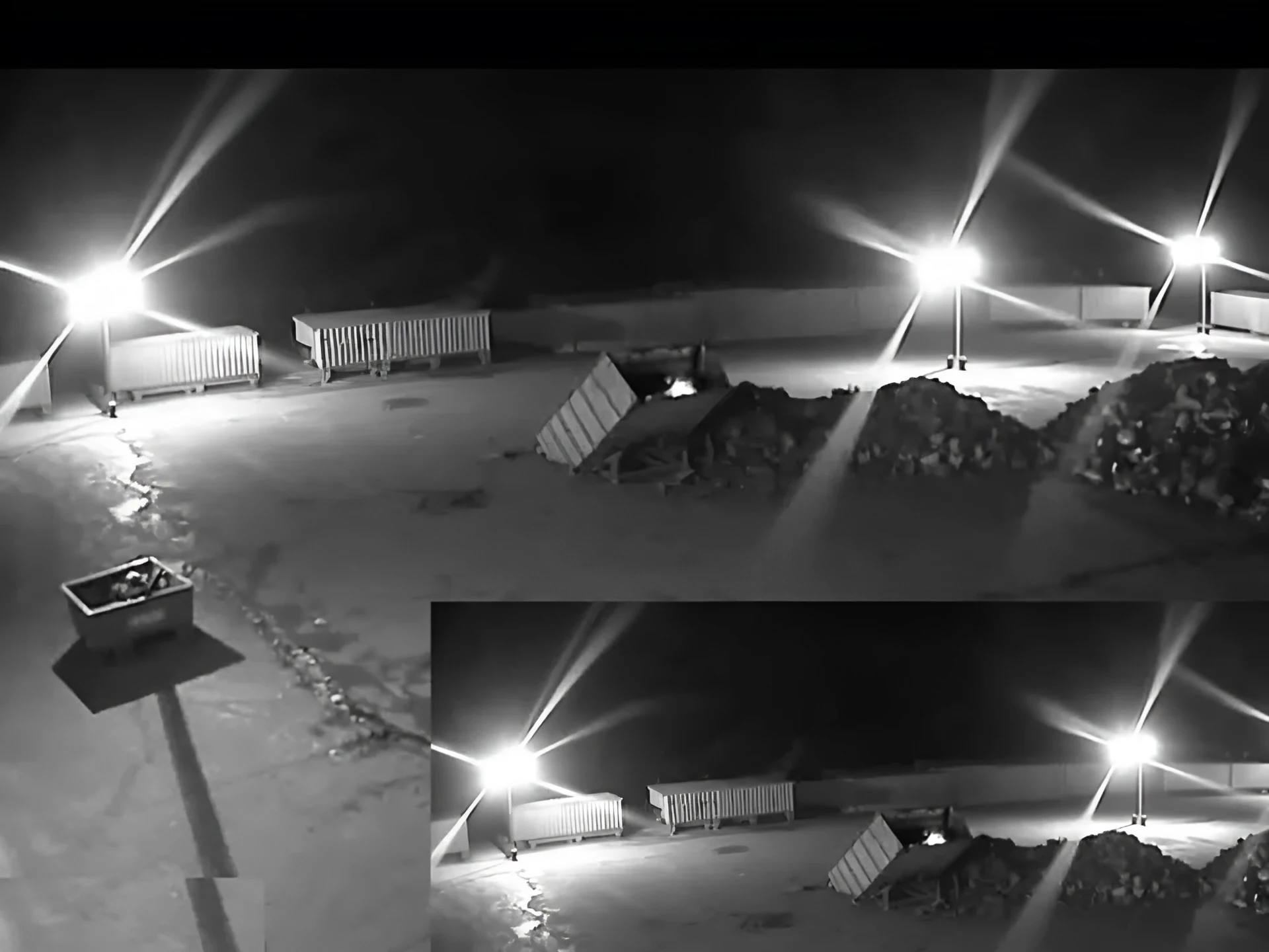Real night-time CCTV frame of a storage yard with a small fire starting in a skip, from an existing camera