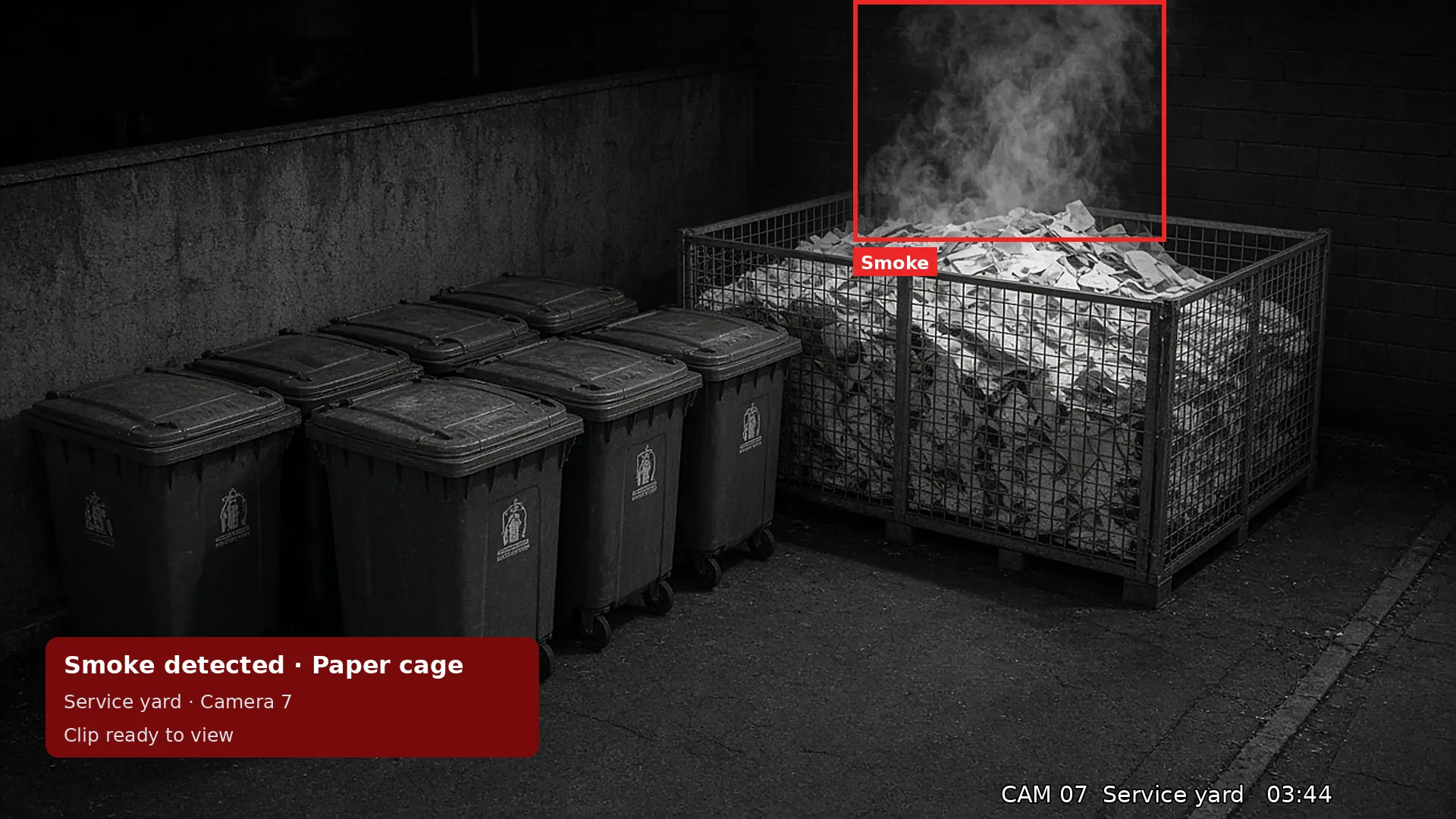 Night IR CCTV of smoke rising from a paper recycling cage beside wheelie bins, boxed by AI